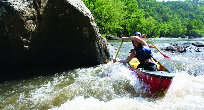 Two people waring safety gear navigate a canoe through whitewater. 